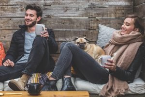 Man and woman with dog in her lap sitting with cups in their hands