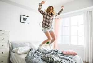 A woman jumping on a bed with joy. You can remodel your bedroom to improve your own happiness.