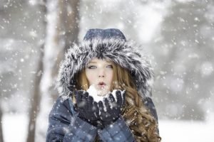 A girl in winter jacket blowing snow 